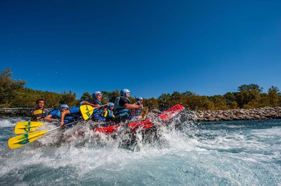 A WeRoad group trip paddling through white water rapids in a red inflatable raft under a clear blue sky.