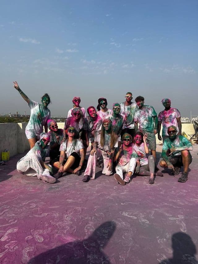 Un gruppo WeRoad sorride per una foto su una terrazza, cosparso di polvere colorata rosa e verde di un festival.