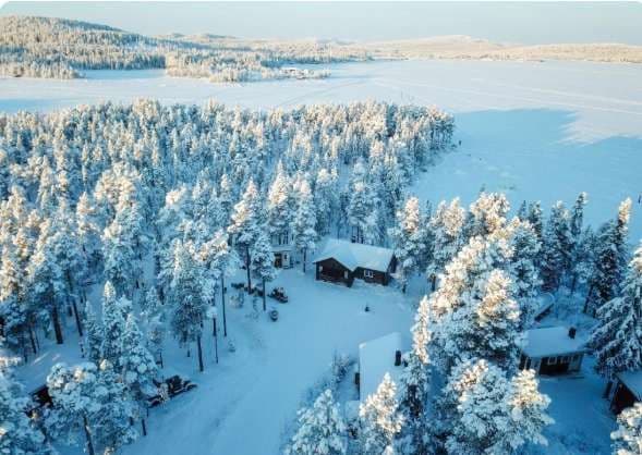 Una vista aérea de cabañas de madera en un bosque de pinos cubierto de nieve junto a un lago helado.