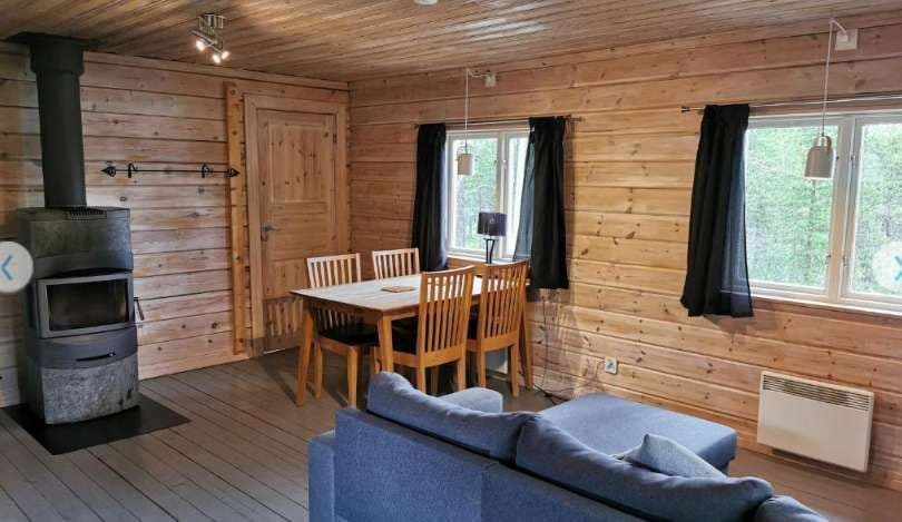 Das Innere einer Holzhütte mit Esstisch, blauem Sofa und Holzofen.