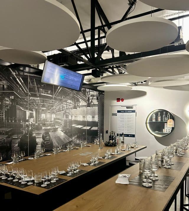 Largas mesas de madera con numerosas copas vacías en una moderna sala de catas con un mural industrial en blanco y negro en la pared.