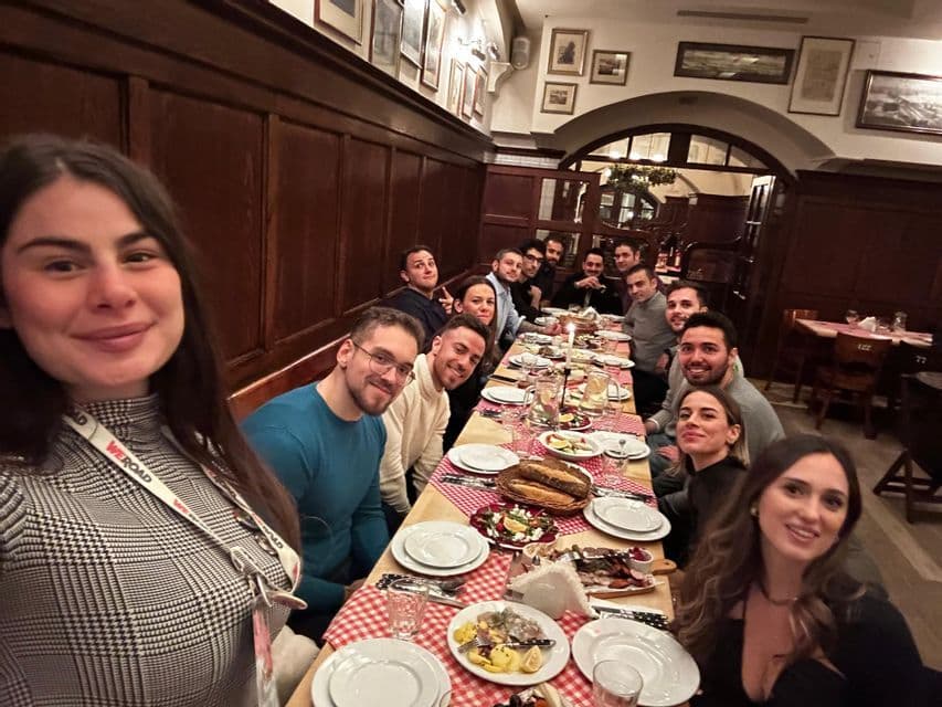 Un grupo de WeRoad se toma una selfi sentado en una larga mesa de un restaurante con paneles de madera.