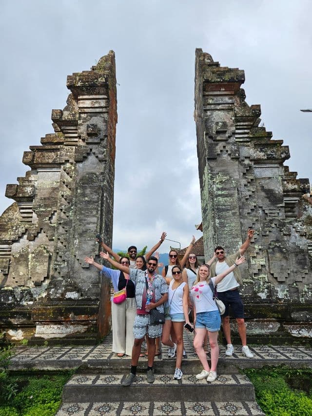 Un groupe WeRoad en voyage pose pour une photo sur des marches, entre deux grandes portes traditionnelles en pierre sculptée.