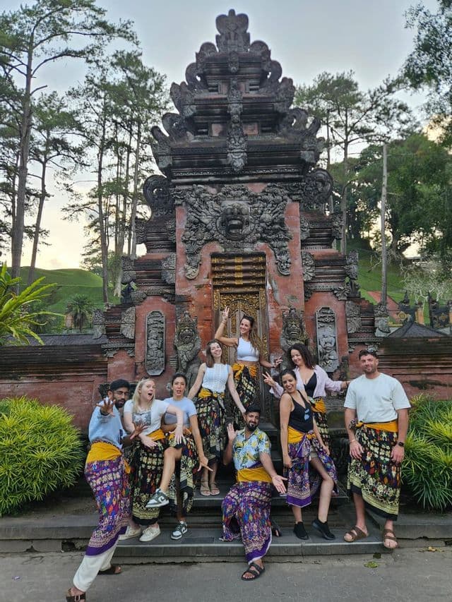 A WeRoad group trip of people wearing colorful sarongs posing for a photo on the steps of an ornate stone temple.