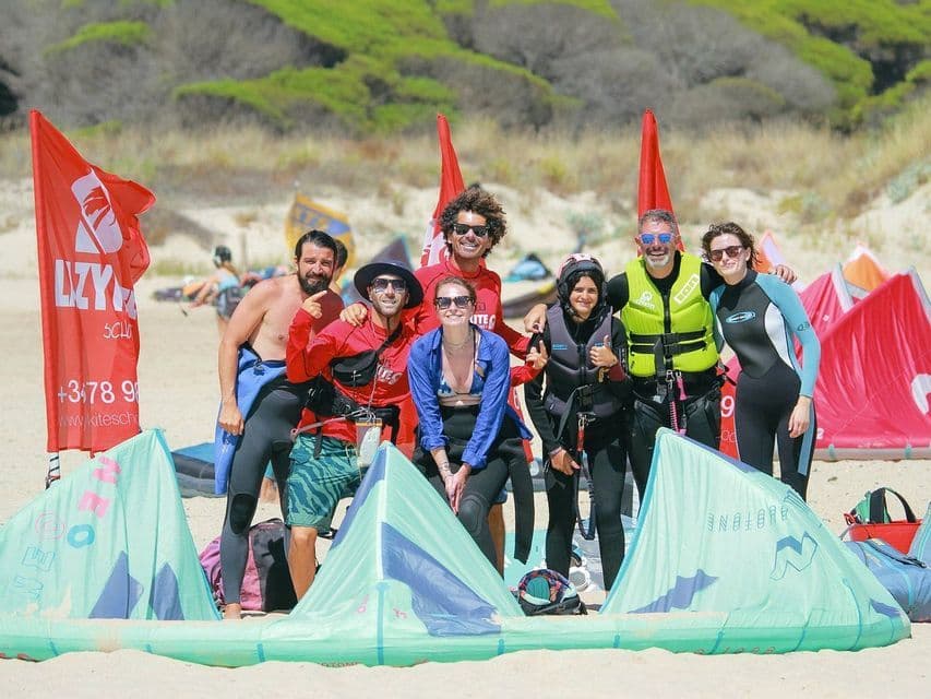 Un viaje en grupo de WeRoad posando para una foto en una playa de arena con su equipo de kitesurf.