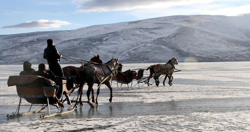 Un viaggio di gruppo WeRoad in slitta trainata da cavalli su un lago ghiacciato con una grande montagna innevata sullo sfondo.