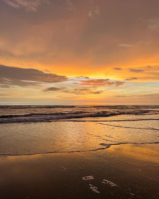 Un coucher de soleil orange éclatant sur l'océan, avec sa lumière se reflétant sur le sable mouillé tandis que les vagues lèchent doucement le rivage.