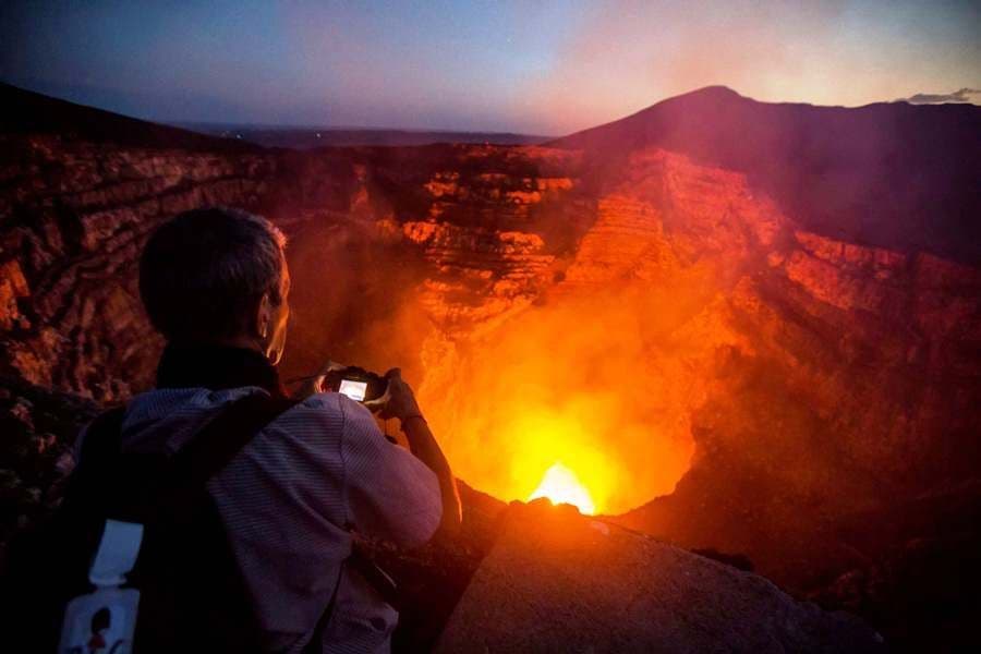 Un randonneur photographie la lave incandescente d'un cratère volcanique au crépuscule.