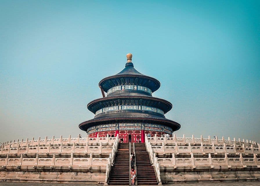 Eine Untersicht auf einen traditionellen, dreistöckigen chinesischen Tempel mit blauem Dach, der auf einer breiten Steintreppe unter einem klaren blauen Himmel steht.
