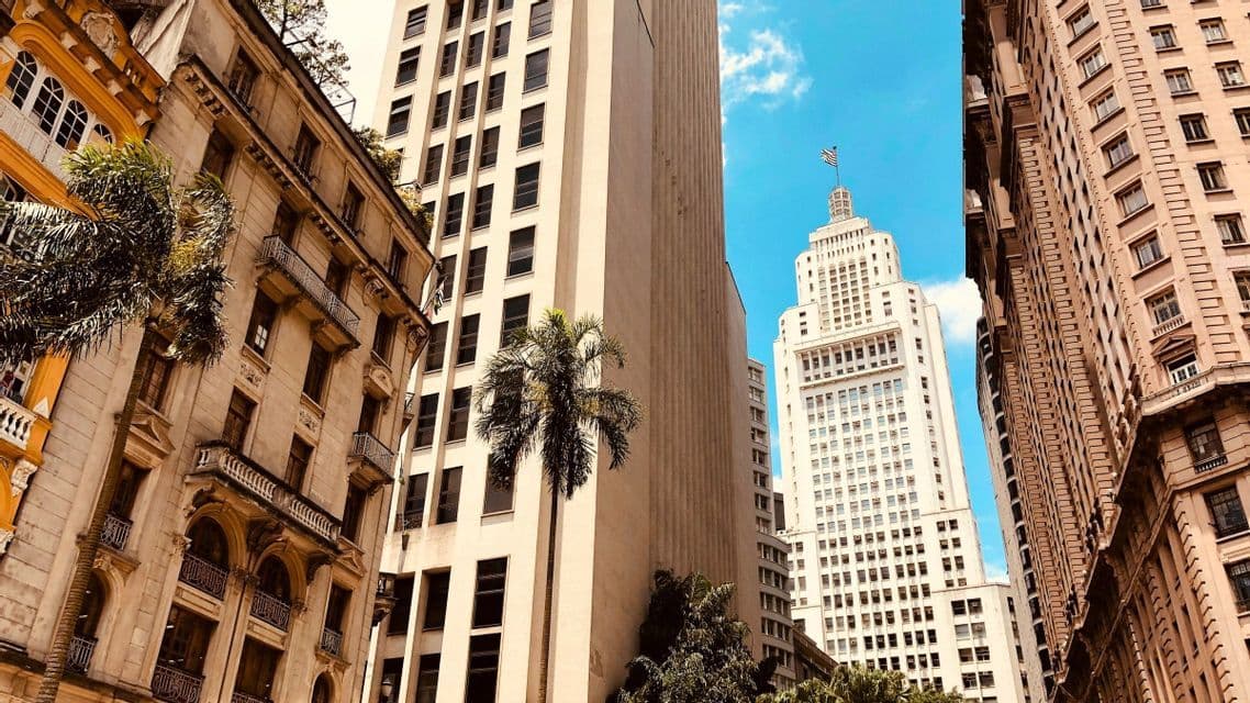 Moderne und klassische Wolkenkratzer ragen vor einem strahlend blauen Himmel empor, dazwischen ist eine Palme zu sehen.