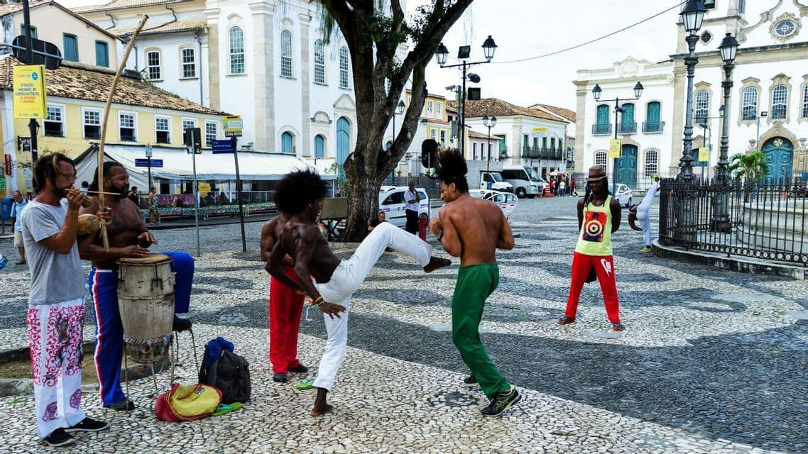 Eine Gruppe Straßenkünstler praktiziert Capoeira und musiziert auf einem gepflasterten Stadtplatz.