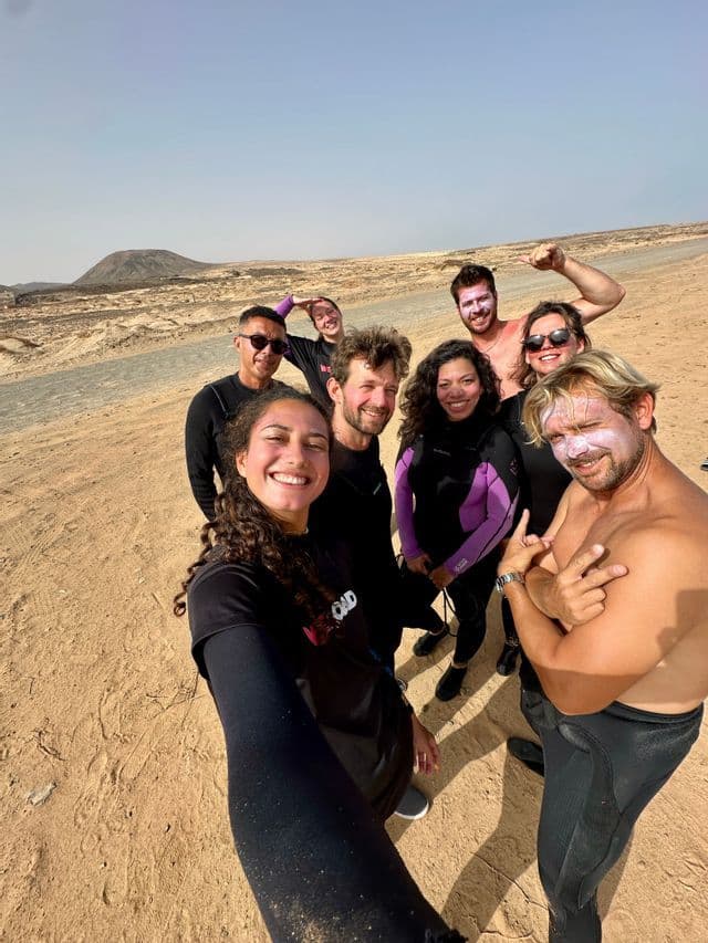 Un voyage de groupe WeRoad en combinaisons de plongée prend la pose pour un selfie dans un paysage désertique avec une colline lointaine.