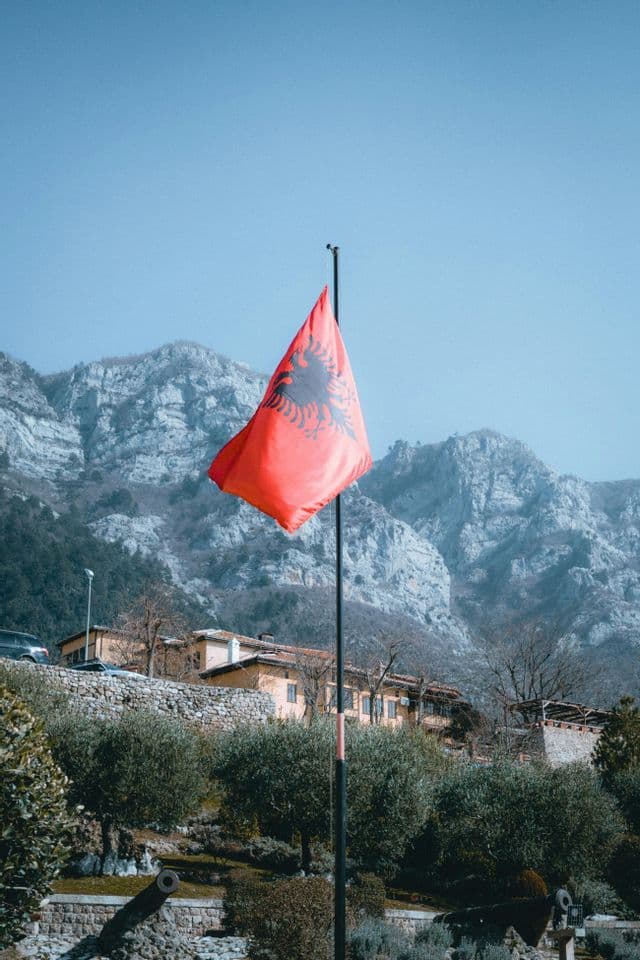 Le drapeau albanais flottant sur un mât avec une chaîne de montagnes escarpées en arrière-plan.
