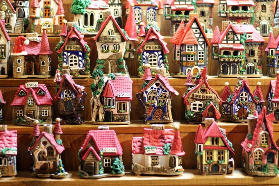 A collection of small, colorful ceramic souvenir houses with red roofs arranged on wooden shelves.