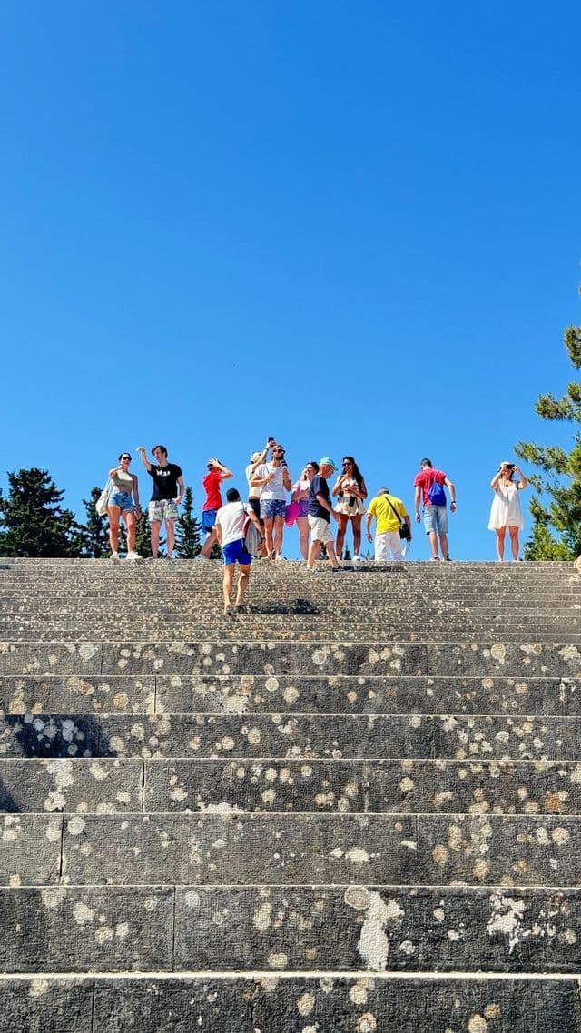Un gruppo WeRoad in cima a un'ampia scalinata in pietra consumata, visto dal basso sotto un cielo azzurro.