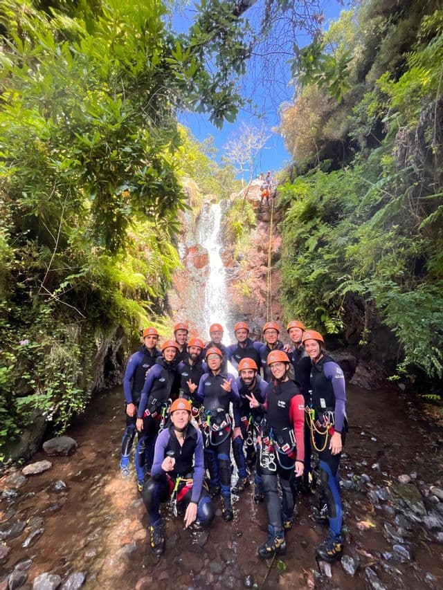 Un viaggio di gruppo WeRoad con mute e caschi posa per una foto in un ruscello alla base di una cascata durante un'attività di canyoning.