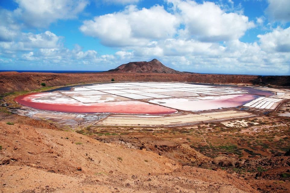 Un'ampia vista di saline rosa e bianche in un cratere vulcanico, con una montagna e l'oceano sullo sfondo.