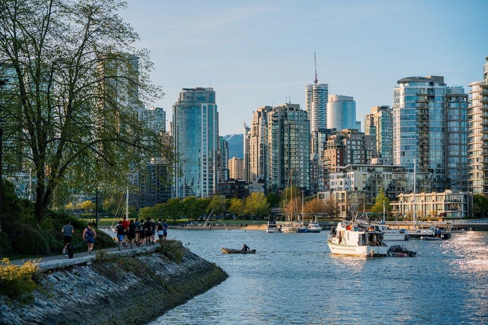 Un gruppo di persone fa jogging su un percorso lungomare, con barche sull'acqua e uno skyline moderno della città dietro di loro.