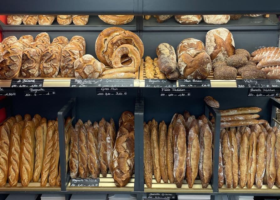 A variety of freshly baked breads, including baguettes and artisanal loaves, displayed on shelves in a bakery.