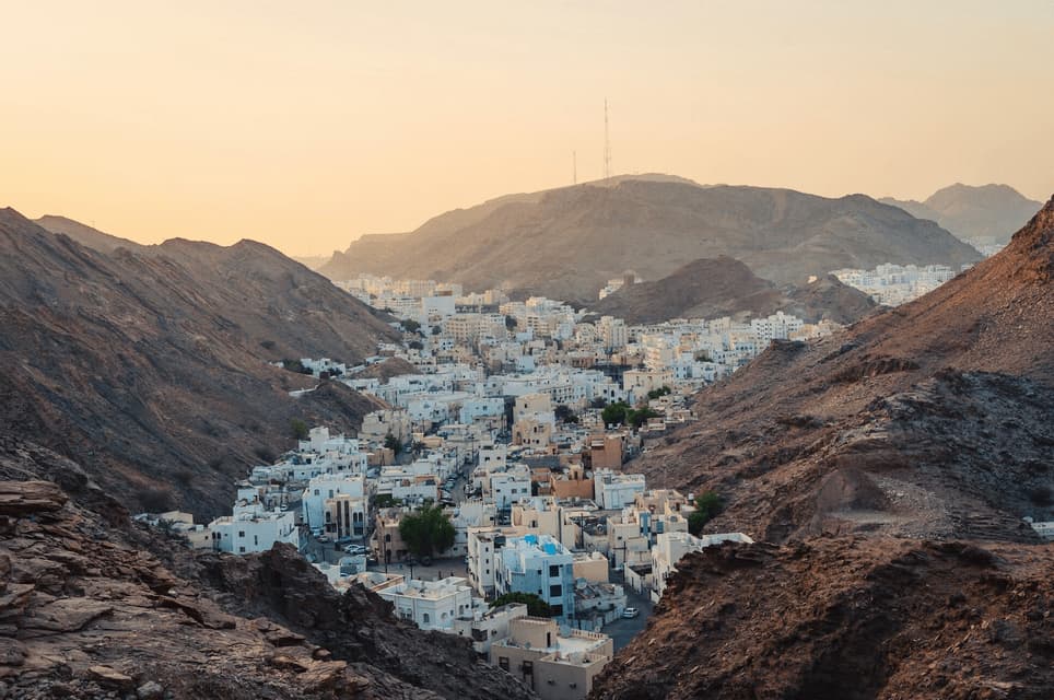 A high-angle view of a city with white buildings nestled in a rocky mountain valley at sunset.