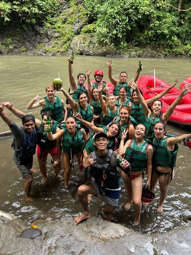 Un viaggio di gruppo WeRoad: persone in giubbotti di salvataggio sorridono e posano in un fiume, con bevande in mano e zattere rosse sullo sfondo.