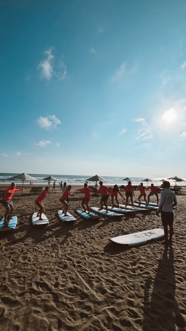 Un viaggio di gruppo WeRoad impara a fare surf, provando a stare in piedi sulla tavola su una spiaggia assolata con un istruttore.