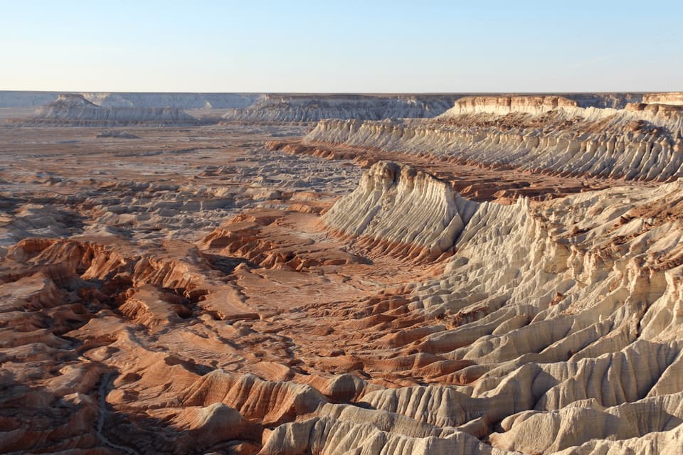 Un vasto paesaggio di formazioni rocciose erose bianche e rosse in un canyon desertico sotto un cielo sereno.