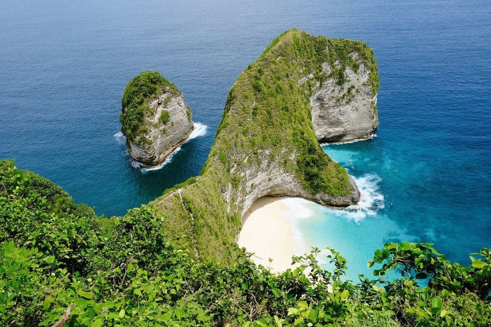 Una veduta dall'alto di una grande scogliera ricoperta di verde che circonda una spiaggia isolata di sabbia bianca e un mare turchese.