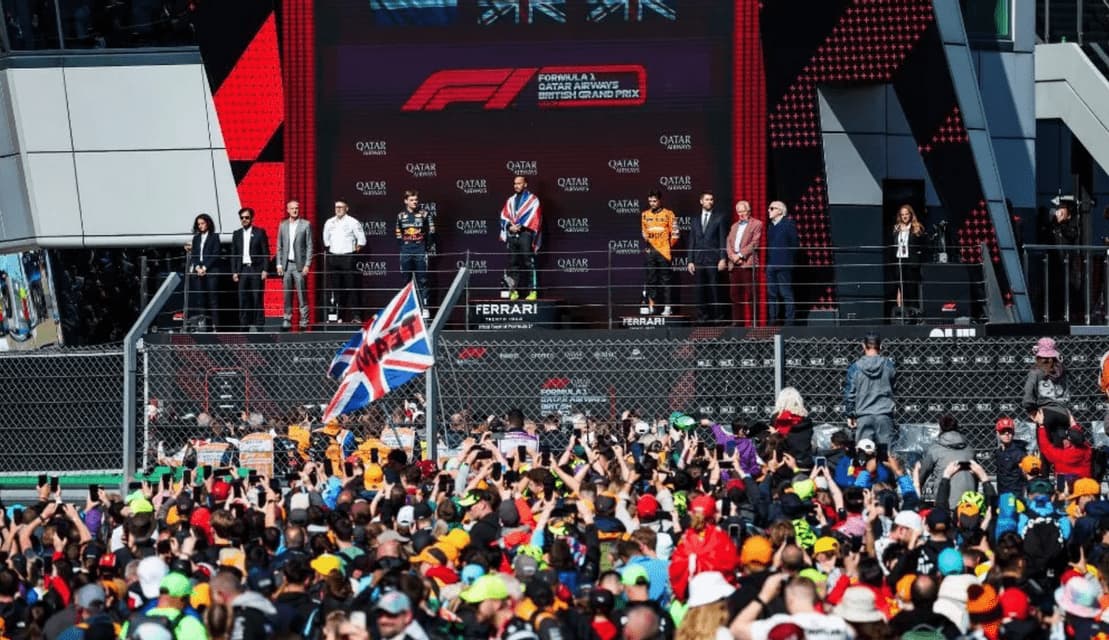 Formula 1 drivers celebrate on the podium as a large crowd cheers below at the British Grand Prix.