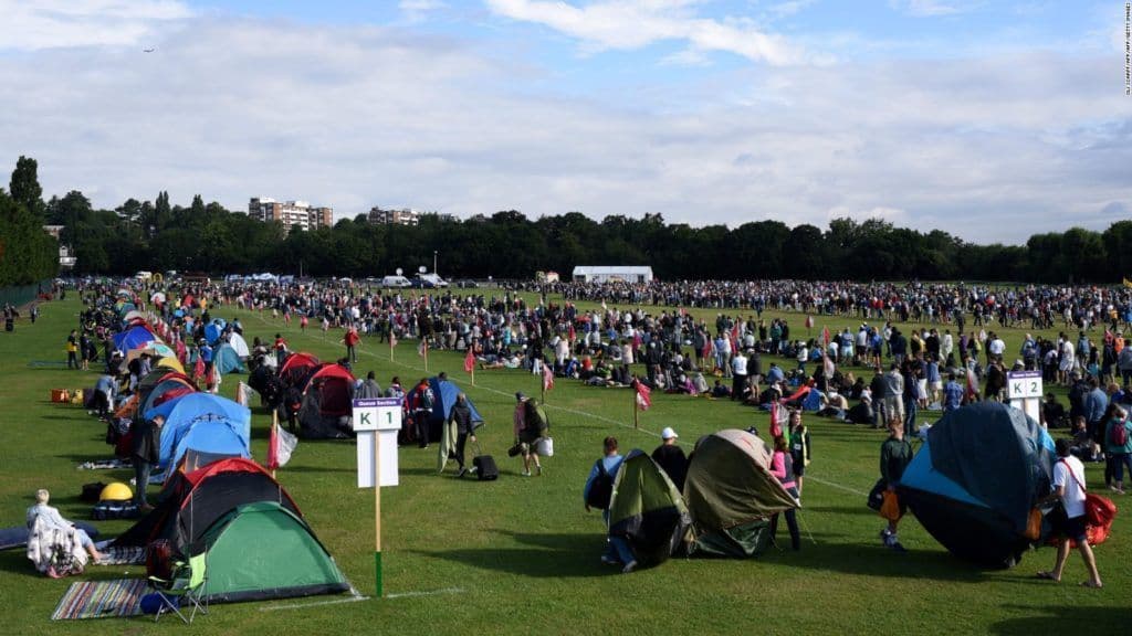 A large crowd of people with colorful tents set up in rows on a vast green field during an outdoor event.
