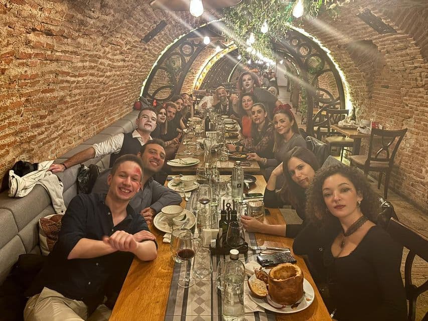 Un gruppo WeRoad, in costume e trucco, che sorride a una lunga tavolata all'interno di un ristorante con pareti in mattoni ad arco.