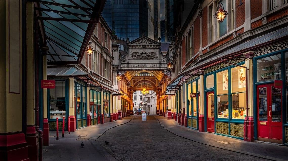 Eine ruhige, gepflasterte Gasse im Leadenhall Market, mit beleuchteten Ladenfronten unter einem verzierten, überdachten Dach in der Dämmerung.