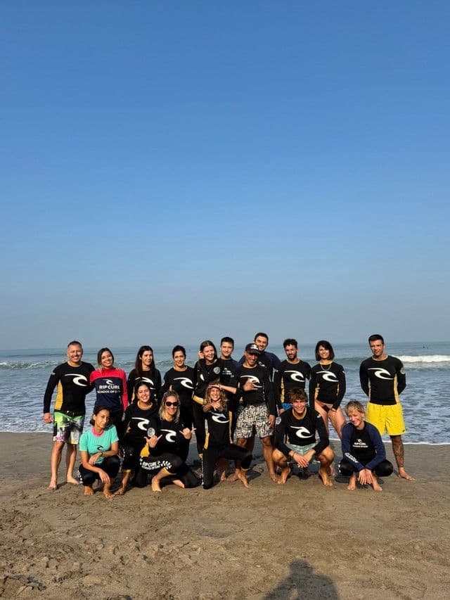 Un viaggio di gruppo WeRoad in mute da sub posa per una foto su una spiaggia sabbiosa con l'oceano sullo sfondo.