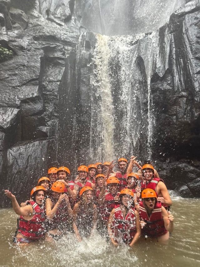 Un viaggio di gruppo WeRoad con caschi e giubbotti di salvataggio sorride e posa insieme nell'acqua ai piedi di una grande cascata.