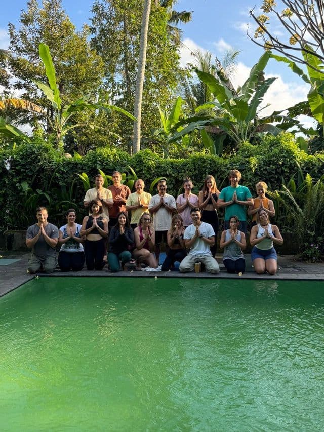 Un gruppo WeRoad in viaggio posa con le mani unite a bordo piscina davanti a un rigoglioso giardino tropicale.