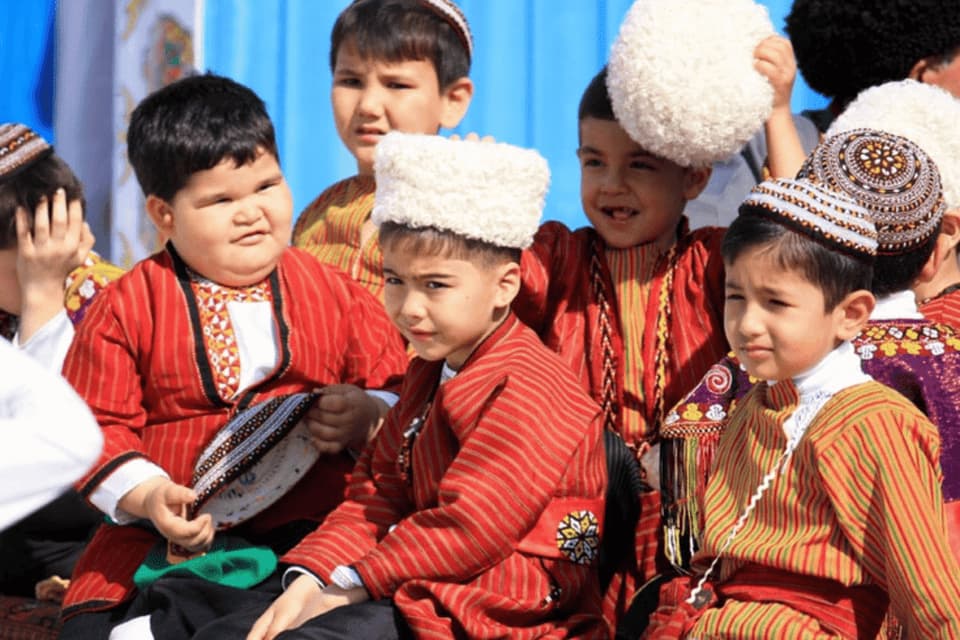 Un gruppo di giovani ragazzi, che indossano vesti tradizionali a righe colorate e cappelli di stili diversi, sono seduti vicini.