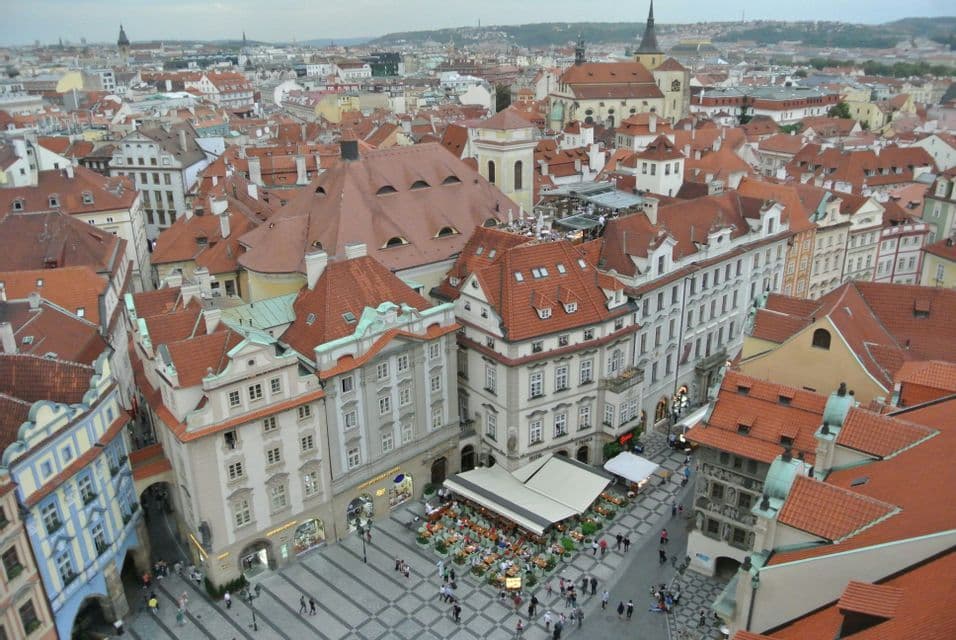 Una vista aérea de una plaza de ciudad europea rodeada de edificios históricos con tejados de tejas rojas y gente caminando abajo.