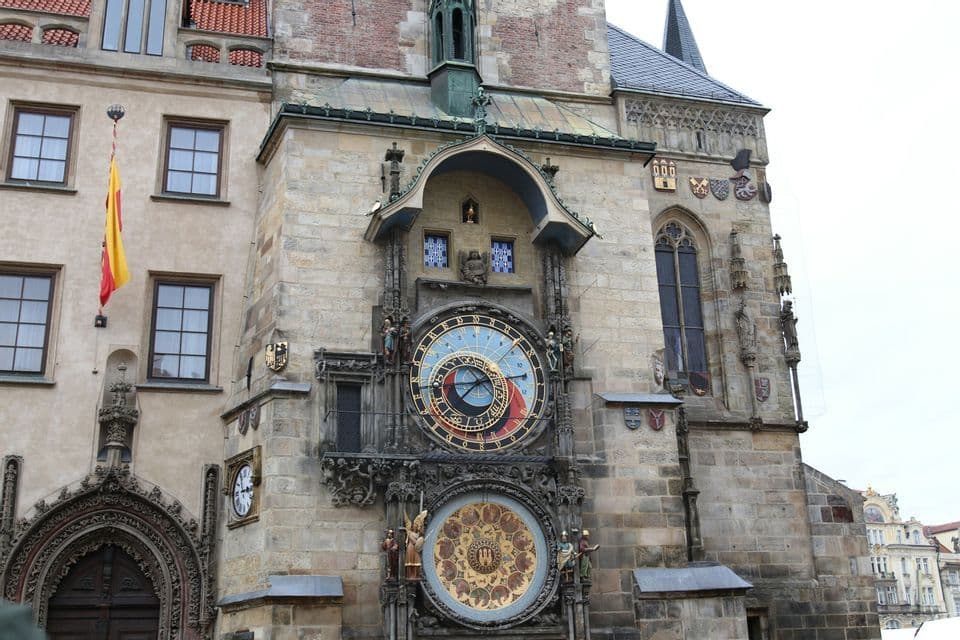 Un primer plano de un ornamentado reloj astronómico medieval con dos esferas grandes y detalladas en la fachada de una torre de piedra.