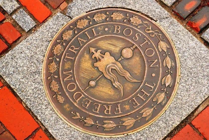 Un medaglione di bronzo che segna il Freedom Trail a Boston, incastonato in un marciapiede di mattoni rossi e granito.