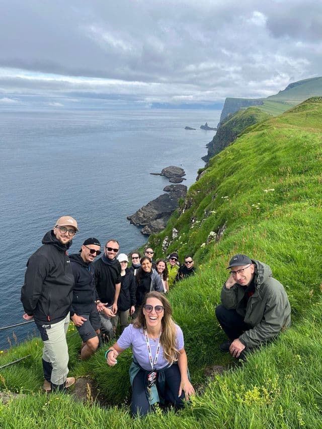 Un gruppo WeRoad in posa per una foto su un ripido sentiero erboso a picco sull'oceano.
