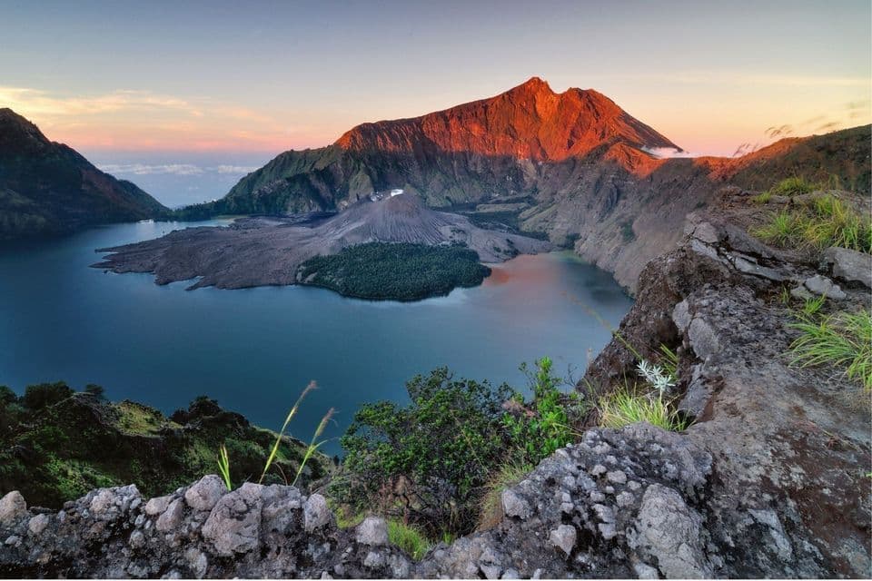 Ein Panoramablick auf eine vulkanische Caldera mit einem großen See und einem zentralen Kegel, beleuchtet vom Sonnenaufgang.