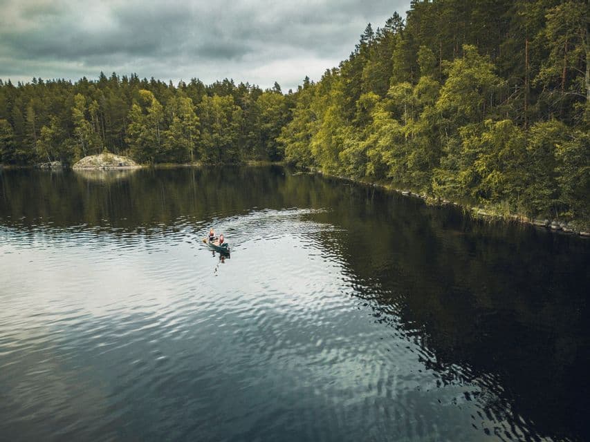 Eine Luftaufnahme von zwei Personen in einem Kanu auf einem ruhigen See, umgeben von dichtem grünen Wald unter bewölktem Himmel.