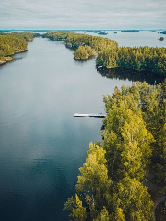 Eine Luftaufnahme eines Sees, der mit zahlreichen bewaldeten Inseln übersät ist, mit einem kleinen weißen Steg, der vom Ufer ins Wasser ragt.