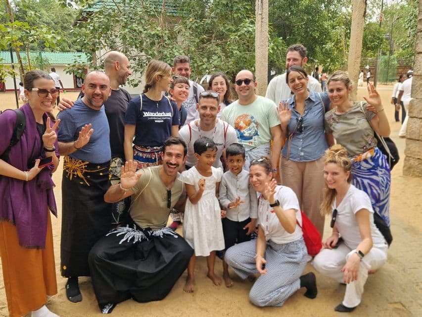 Un gruppo WeRoad in viaggio posa per una foto con due bambini locali, sorridenti e che salutano all'aperto.