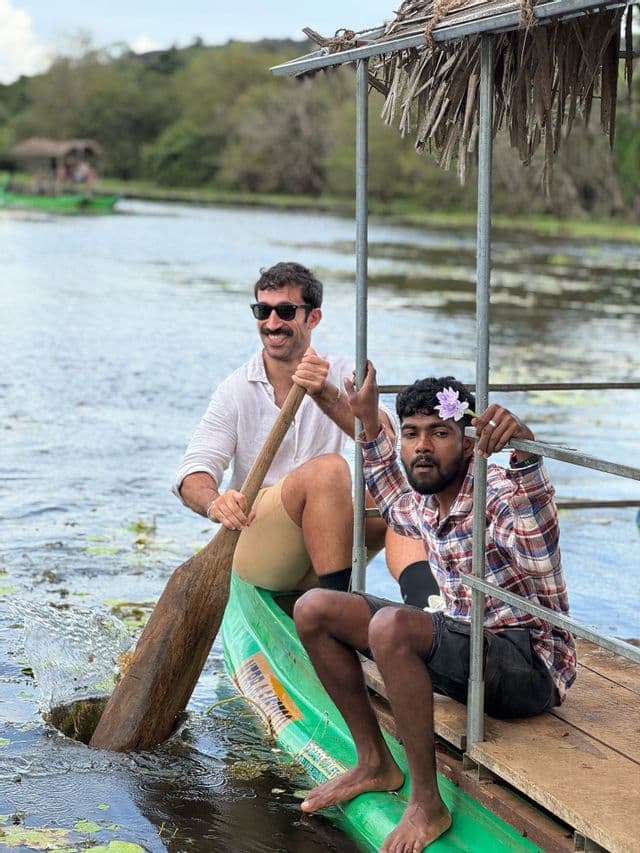 Due uomini di un viaggio di gruppo WeRoad in canoa verde su un lago, uno che pagaia e l'altro seduto sulla piattaforma.
