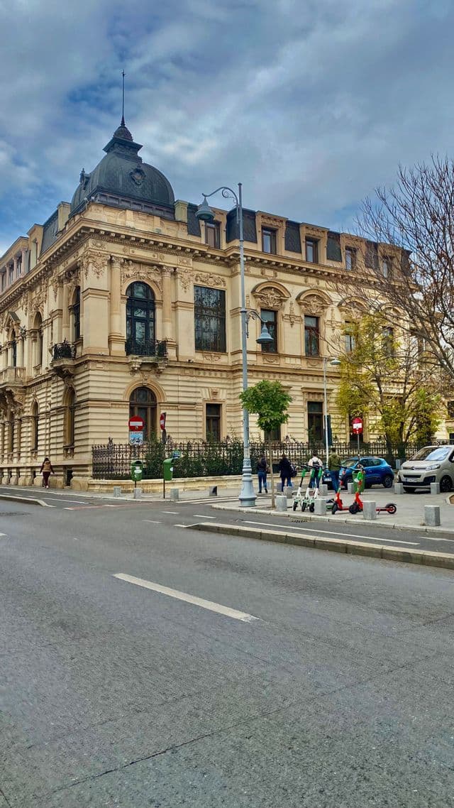 Un edificio ornamentado de estilo clásico con un techo abovedado oscuro en la esquina de una calle de la ciudad bajo un cielo nublado.