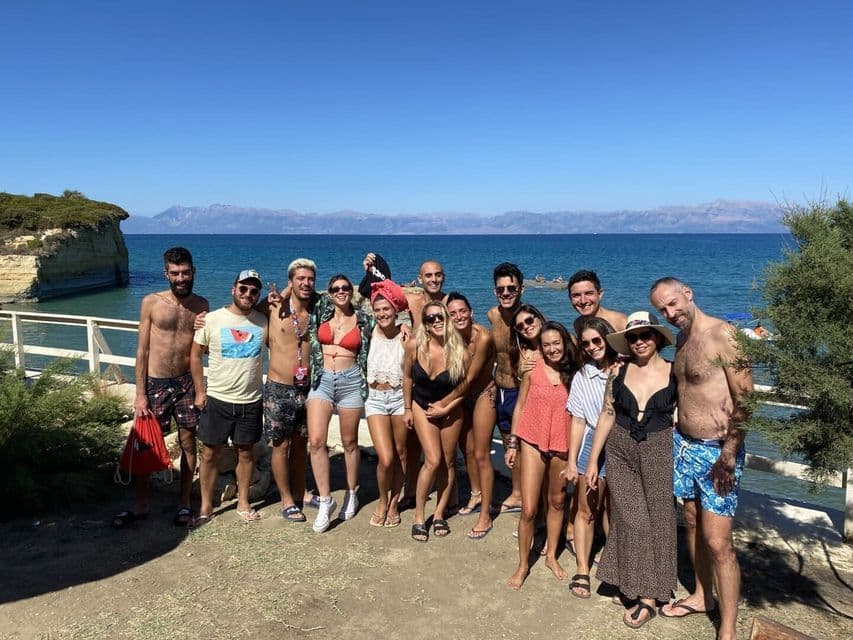 Un gruppo WeRoad in viaggio che si fa una foto in una giornata di sole al mare, con scogliere costiere sullo sfondo.