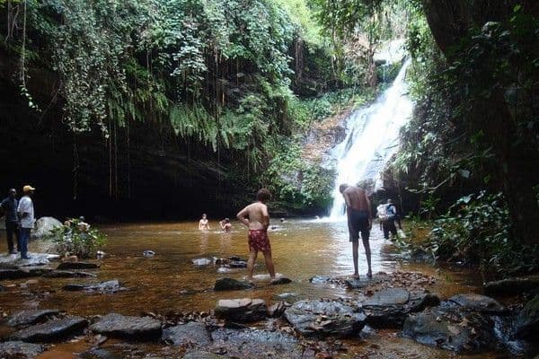 Un viaggio di gruppo WeRoad con persone che nuotano e si rilassano in una piscina naturale ai piedi di una cascata, circondata da una vegetazione lussureggiante.