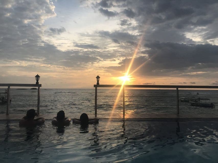 Un voyage en groupe WeRoad de trois personnes se relaxant dans une piscine à débordement tout en regardant le coucher de soleil sur l'océan.