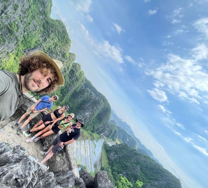 Un uomo si scatta un selfie con il suo gruppo WeRoad durante un viaggio, da un punto panoramico di montagna che domina una vasta valle verde.